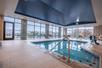 A light blue indoor swimming pool with steps to get in and floor to ceiling windows on the far left and right walls letting daylight in.