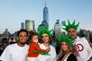 Four adults and a baby posing for a photo, three of them wearing statue of liberty hats, with NYC in the background.