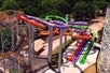 A vibrant water slide complex with multiple twisting slides in various colors, set against a backdrop of lush trees and a clear sky.