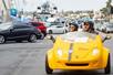 A man and woman wearing sunglasses and black helmets while driving a yellow GoCar and looking at the sights on the GoCar San Diego Harbor and Gaslamp Quarter Tour.