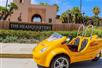 A bright yellow GoCar parked in front of the well landscaped sign for The Headquarters At Seaport District on a sunny day.