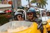Close up of a man and woman wearing helmets having fun and driving a bright yellow GoCar with another GoCar behind them.