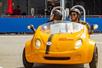 A man and woman wearing black helmets and laughing while driving a yellow GoCar on a sunny day in San Diego.