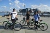 Three tourists holding a bike from Boston Bike Rental and Boston skyscraper on the background with Boston Explorer Pass by Go City.
