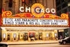 The marquee of the Chicago Theatre advertising a concert by Ringo Starr & His All Starr Band, indicates that the event is presented by Elite and Parachute Concerts and a  lively atmosphere of the city at night.