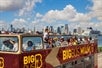 Red double decker bus by Big Bus Tour with several people aboard on it and a beautiful Miami skyscraper on the background with Go Miami All-Inclusive Pass.