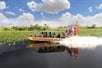 An airboat with a name "Everglades Holiday Park" printed on it with several people aboard on Big Bus Miami Everglades Tour with with Go Miami All-Inclusive Pass.

