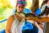 A girl holding a lizard, taken at the Cajun Pride Swamp Tours. The girl is wearing sunglasses and is outdoors.