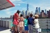 A group of children accompanied by a woman enjoy the view of New York City's skyscrapers from aboard a ferry on the water.
