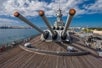 The imposing view of the USS Missouri's three large cannons, set against a backdrop of calm waters and a clear sky at Pearl Harbor.