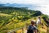 A view from the Diamond Head hike in Hawaii, showing hikers descending a staircase with lush greenery and a stunning ocean view in the background.