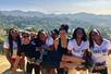 A group of woman holding a man in front of them and posing for a photo with Griffith Park behind them on a sunny day.