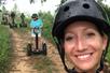 A woman in a black helmet taking a selfie with group of tourists riding the segways on a dirt path behind her.