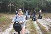A group of tourists on segways in a rocky clearing with tall green trees behind them on the Guided Segway Tour of Lake Louisa State Park.
