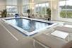 An indoor swimming pool in a room with large windows and lounge chairs around three sides at the HYATT House Pittsburgh-South Side.