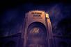 The concrete arch front entrance of Universal Studios Hollywood with dark purple fog around it and spooky leafless trees in the background.