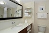 A lighted mirror, towels, toiletries and sink inside a guest bathroom.