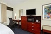 Flat screen TV, mini refrigerator, microwave and a work desk and chair inside a guest room.