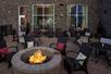 A brick patio with several sets of tables and chairs and a lit fire pit with chairs around it at the Hampton Inn & Suites-Asheville Biltmore Village.