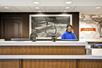 A tall brown front desk with white counter tops with a clerk on the phone behind it and a treats section at the Hampton Inn & Suites Columbus-Easton Area.