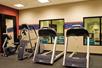 A small fitness center with two treadmills, an elliptical, and a stationary bike in front of windows that show in an indoor pool.
