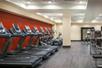 A fitness center with a row of cardio equipment in front of a red wall on the left side and a weights area with several machines on the right.