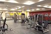 A fitness center with a large weights area with several machines and a row of cardio equipment along the red wall to the right.