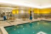 A large indoor swimming pool with several sets of tables and chairs along the sides and a hot tub to the left of it.