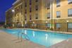 A light blue outdoor swimming pool with chairs and tables on the side at the Hampton Inn & Suites New Braunfels at dusk.