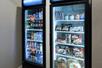Two black refrigerators with glass doors, one full of drinks, the other full of frozen foods and treats.