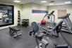A small fitness center with several pieces of cardio equipment, a free weights area, a small window, and a large mirror.