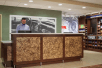 Front desk/reception area with a hotel staff behind the desk and a mini grocery nearby.