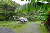 A silver and black Maverick helicopter parked in a gravel patch with a mountain behind them in the Hana Rainforest.
