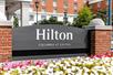Close up of the gray and red brick sign for the Hilton Columbus at Easton with multicolored flowers in front of it on a sunny day.