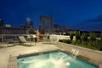 A rooftop hot tub with water flowing into it, lounge chairs on the far side, plants to the right, and the city of Atlanta at dusk in the background.