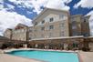 An light blue outdoor swimming pool with chairs on the side and the Hilton Garden Inn New Braunfels behind it on a sunny day.
