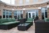 A stone terrace with several sets of green and gray patio furniture in front of a wall of windows at the Hilton Garden Inn New Braunfels.