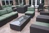 A stone terrace with several sets of green and gray patio furniture and a wall with lots of windows behind them at the Hilton Garden Inn New Braunfels.
