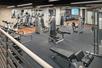 A large fitness center with several rows of cardio equipment with a mirror in front of them and a few weight machines.
