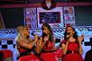 Three women in red dresses sing in a diner setting