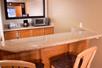 A hotel room wet bar with two bar chairs at it, a microwave, small sink, coffee pot, and a mirror.