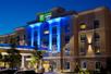 The front exterior of the Holiday Inn Express & Suites at night with blue lights illuminating the center.