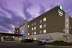 The exterior of the Holiday Inn Express & Suites New Braunfels with cars parking in the front and a purple sky overhead.