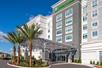 The front exterior and covered entrance of the Holiday Inn & Suites Orlando International Drive South with beautiful landscaping around the entrance.