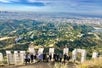 View looking down on a group of hikers standing behind the Hollywood sign with Los Angeles in the distance.