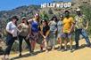 A group of hikers wearing sunglasses standing together for a photo with the Hollywood sign in the background.