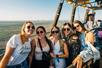 A group of young women wearing sun glasses posing for a photo while in the air in a hot air balloon on a sunny day.