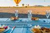 A picnic set with plates of snacks, champagne glasses and cutlery with hot air balloons landing in the background.