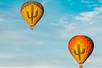 Two yellow hot air balloons with green cacti on them high in the air with a light blue clouded sky behind them.