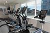 A row of cardio equipment lined up in front of a window showing the city of Denver on a sunny day at the Hotel Indigo Denver Downtown.